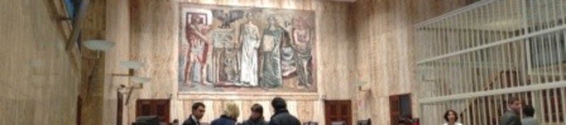 Aula d'assise con l'affresco sulla parete di fondo e la gabbia degli imputati